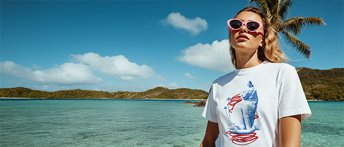 Woman wearing a white t-shirt with a graphic design by the ocean and palm tree
